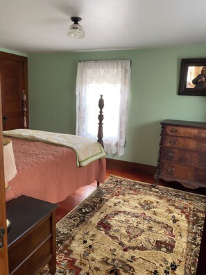 Une pièce comprenant un lit, une commode, une fenêtre ornée de rideaux en dentelle et un ventilateur de plafond.