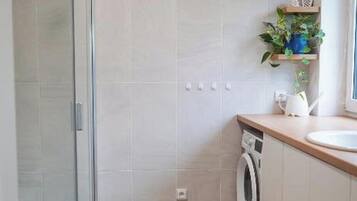 Une salle de bain moderne avec une douche à parois de verre, un lave-linge et un lavabo.