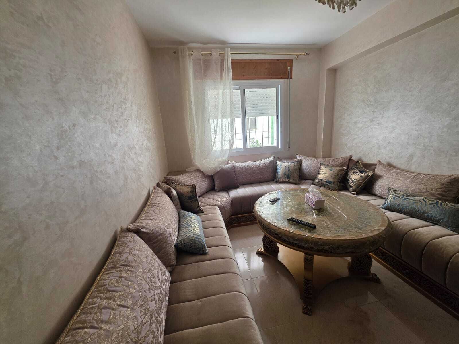 Olohuoneessa on kulmasohva, pyöreä sohvapöytä ja ikkuna, jossa on läpikuultavat verhot.