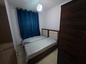 Ein Schlafzimmer mit Bett, Vorhang, Holztür und Deckenleuchte.