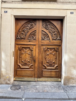 A double wooden door with intricate carvings, set in a beige wall with house numbers 7 and 9. - Studio in a historic building in the heart of the Marais (Paris)