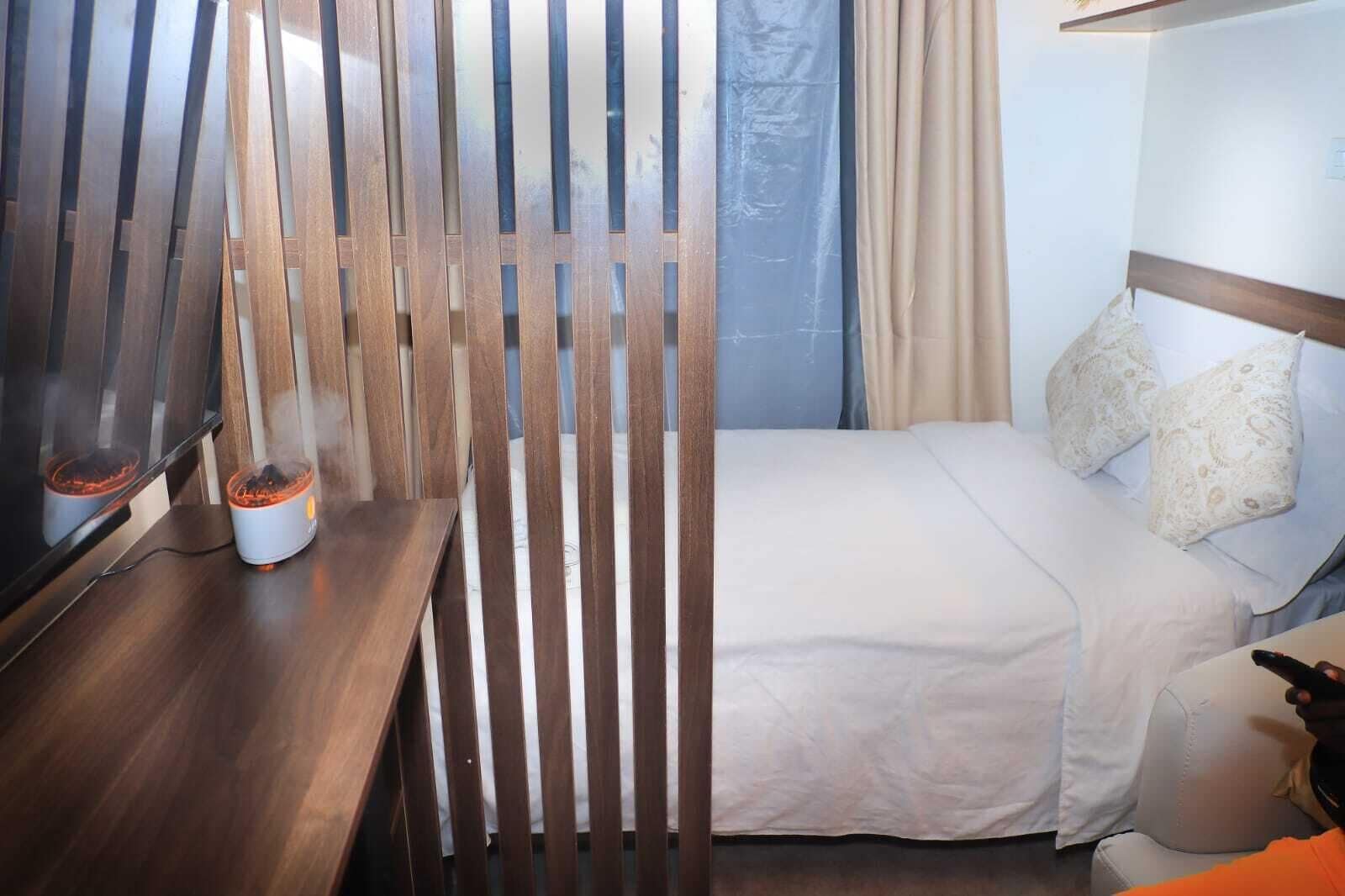 Ein Hotelzimmer mit einem Bett, einem Holzboden, einem Nachttisch mit einem Heizgerät und einem Vorhangfenster.