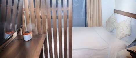 Ein Hotelzimmer mit einem Bett, einem Holzboden, einem Nachttisch mit einem Heizgerät und einem Vorhangfenster.