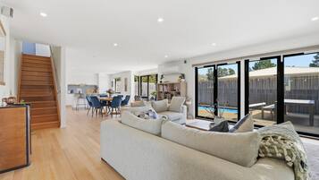 A spacious living area with a large sofa, dining table, and chairs, a staircase leading to an upper level, and a sliding glass door to a pool area.