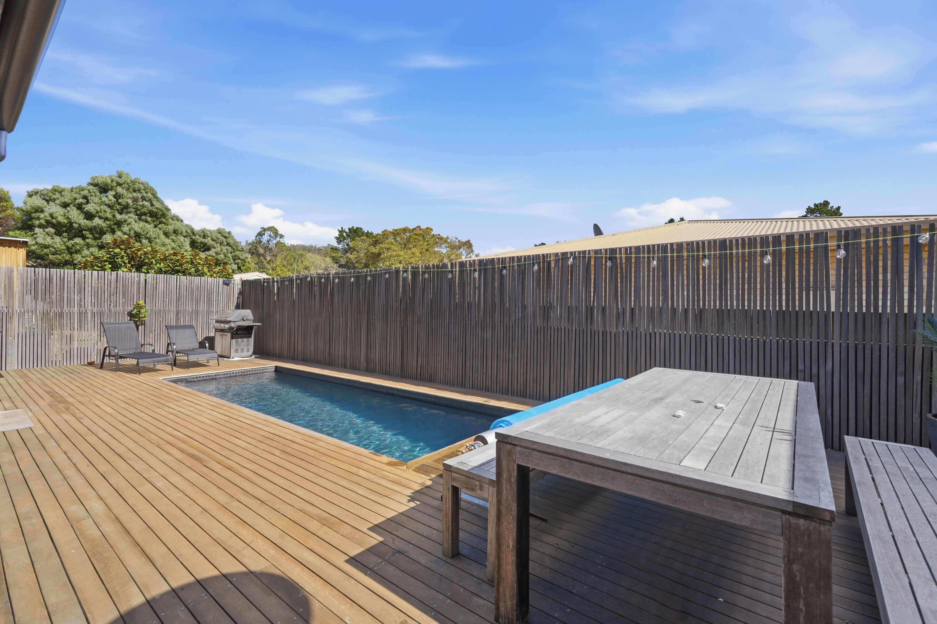 Un pati amb terrassa de fusta, piscina i zona de barbacoa.