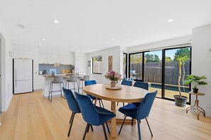 Een moderne keuken met witte kastjes en een eethoek met een ronde tafel en blauwe stoelen.