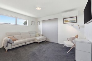 A modern, minimalist room with a grey carpet, a beige sectional sofa, a white desk, and a framed landscape painting.