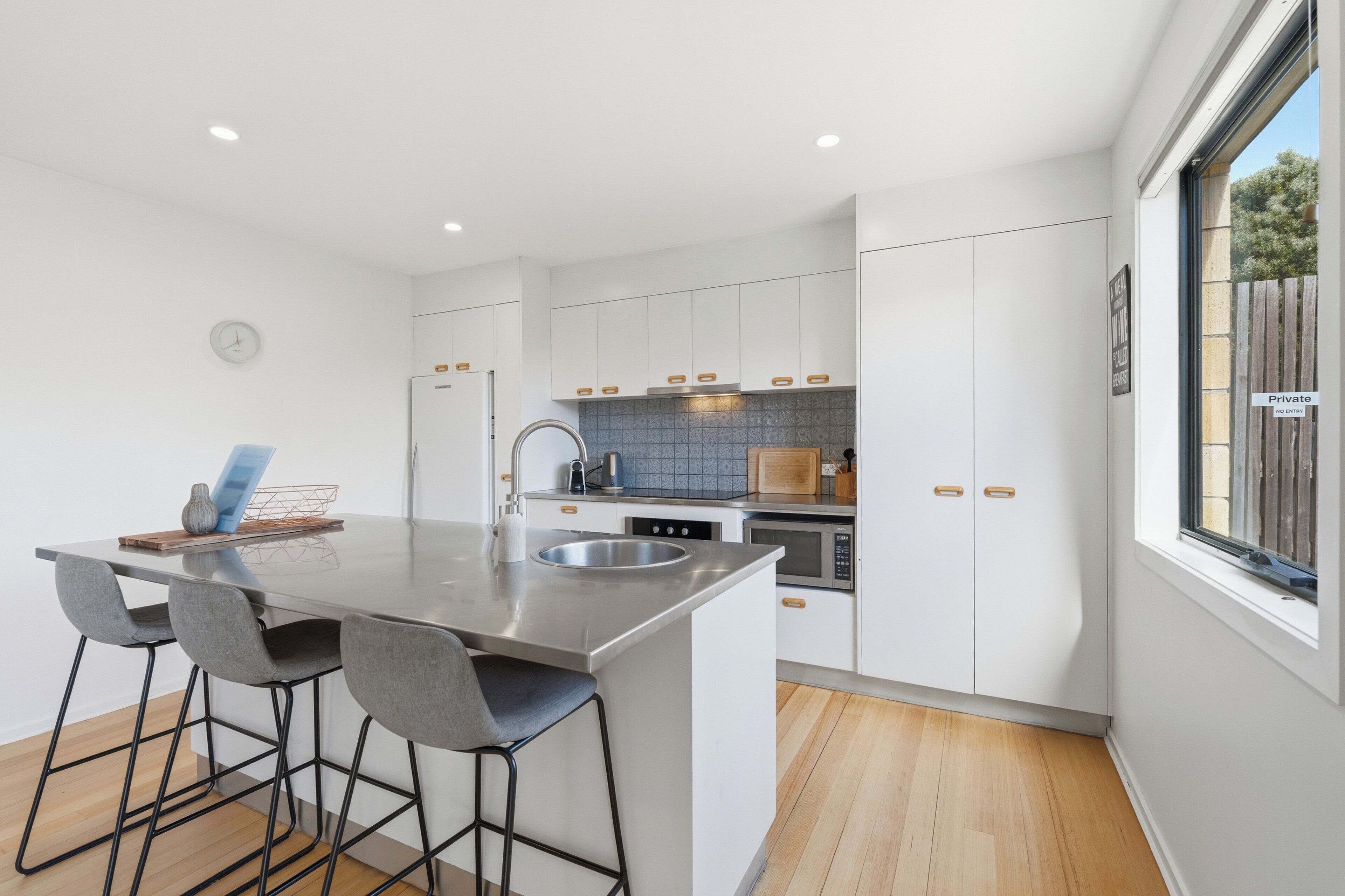 A modern kitchen with a central island, bar stools, a built-in oven, and a window with a view.