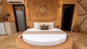 Una cama redonda con colchón blanco y cabecero central con diseño de luna y árbol.