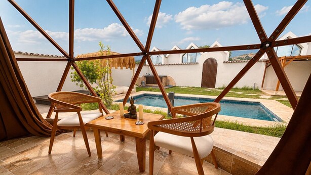 Una habitación con piscina, dos sillas de madera, una mesa y vista a un edificio blanco con una reja.