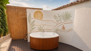 Un área de spa con terraza de madera, bañera redonda y pared decorativa con motivos vegetales.