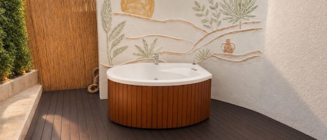 Un área de spa con terraza de madera, bañera redonda y pared decorativa con motivos vegetales.