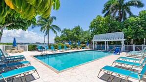 A pool area with blue lounge chairs, a pool, and a covered seating area. - Tradewinds #31 –  Walk to the Beach • Bayfront Community Pool (Bradenton Beach)
