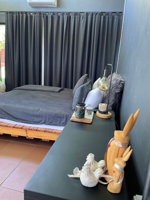 A bedroom with a bed, a bedside table with a lamp, a small figurine, and a window with curtains. - 8 @ Mill Lane • Hartbeespoort Guesthouse • Hot Tub & Mountain Views (Hartbeespoort)