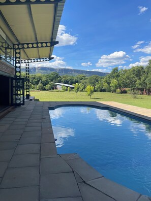 A swimming pool with a patio area, a covered seating structure, and a view of a mountainous landscape. - 8 @ Mill Lane • Hartbeespoort Guesthouse • Hot Tub & Mountain Views (Hartbeespoort)