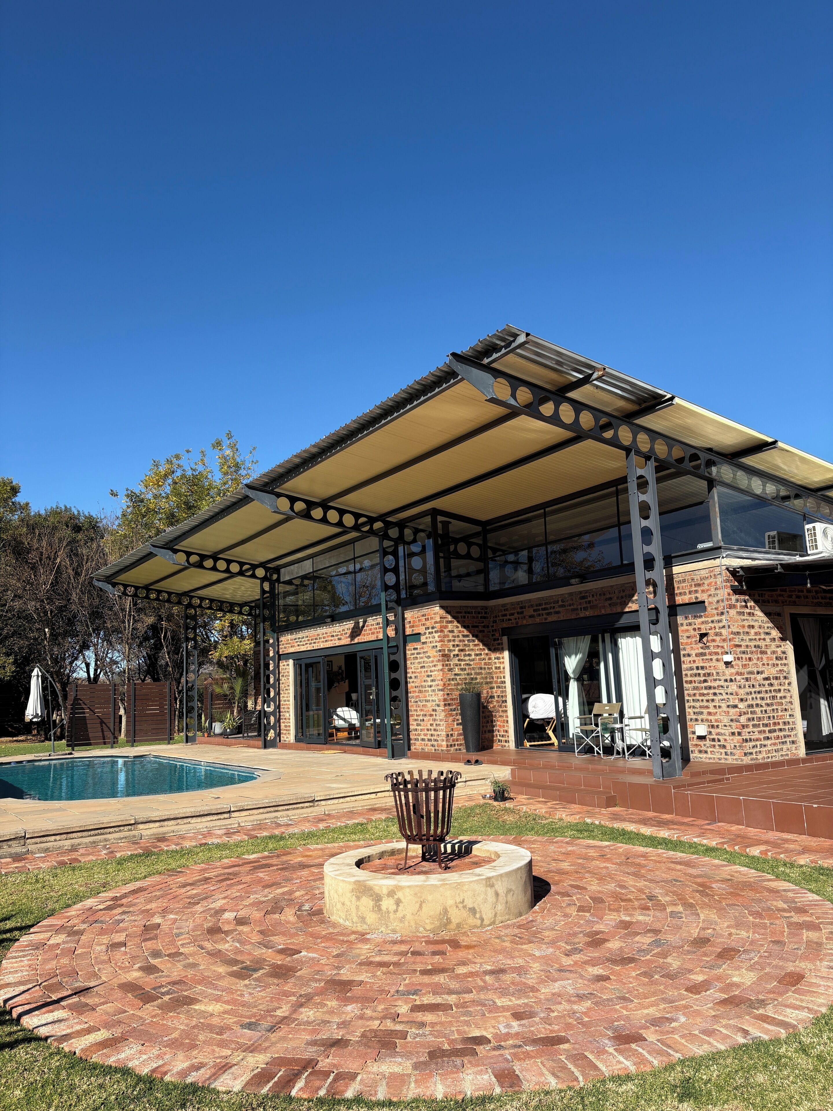 Un espacio exterior techado con piscina, un patio circular de ladrillo y una pérgola.