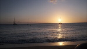 Une mer calme, un coucher de soleil, des bateaux et un horizon dégagé.