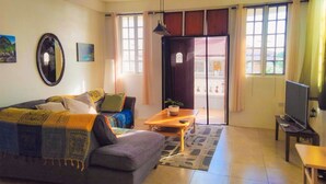 Un salon comprenant un canapé, une table basse, un téléviseur et une porte coulissante donnant sur un balcon.