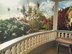 Uma varanda com guarda-corpo branco curvo, uma mesa pequena e diversas plantas e flores.