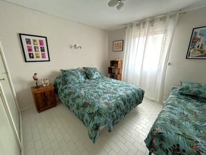 A bedroom with a bed, a nightstand, a small cabinet, and a window with curtains. - Comfortable apartment with air conditioning - 6 guests (Argelès-sur-Mer)