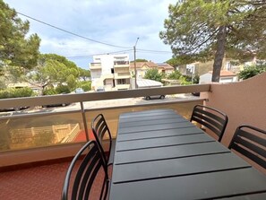 Un balcon avec une table et des chaises, donnant sur un quartier résidentiel avec des immeubles et des arbres.