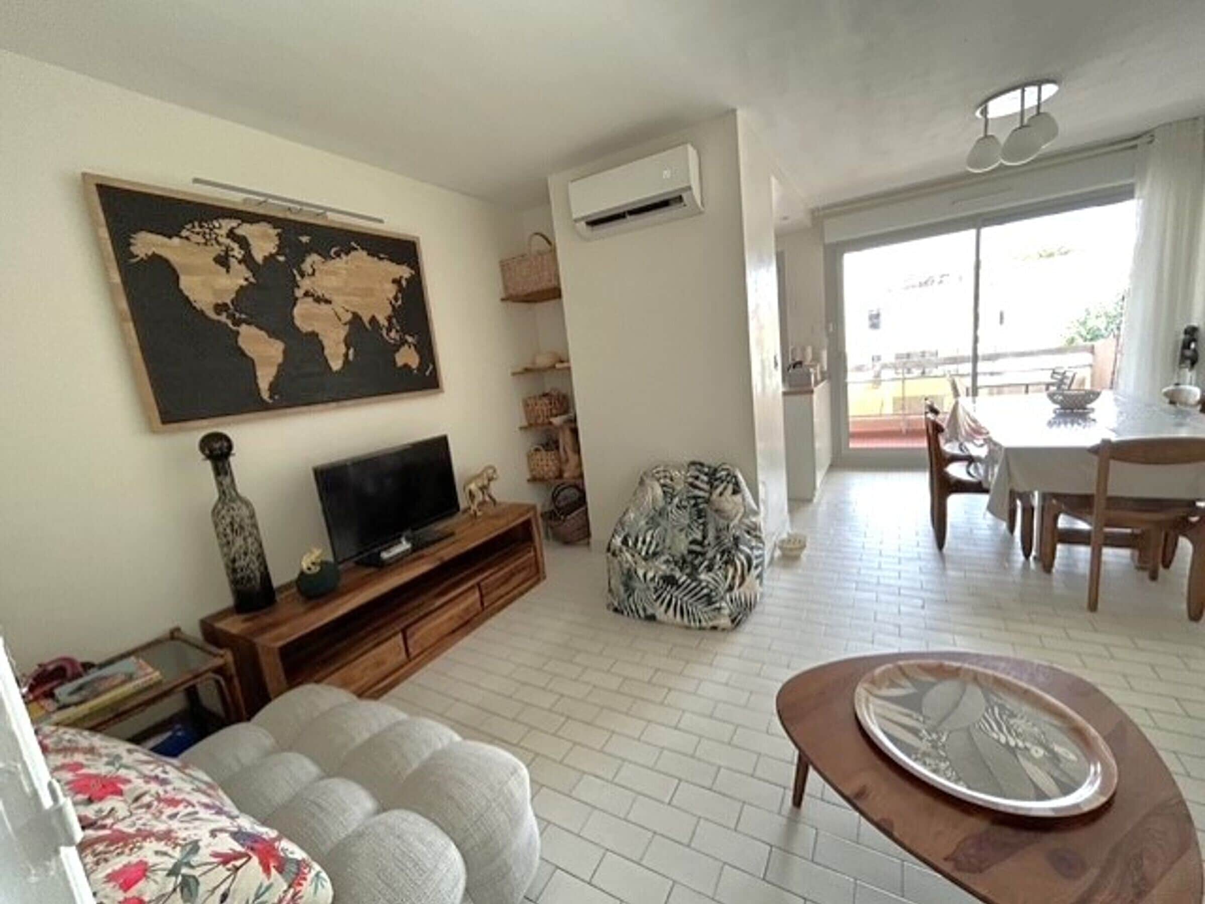 Un salon équipé d’un téléviseur à écran plat, d’une carte du monde, d’un coin repas avec une table et des chaises, et d’un tapis à motifs.