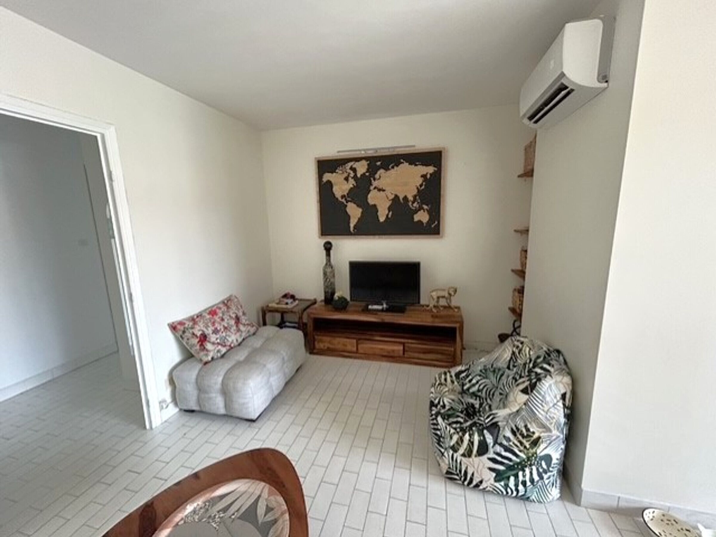 A living room with a sofa, a patterned pouf, a television, a world map on the wall, and an air conditioning unit.