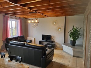 A modern living room with a black leather sofa, a wooden ceiling, a television, and a potted plant. - Cozy house, private parking - 6 guests (Méteren)