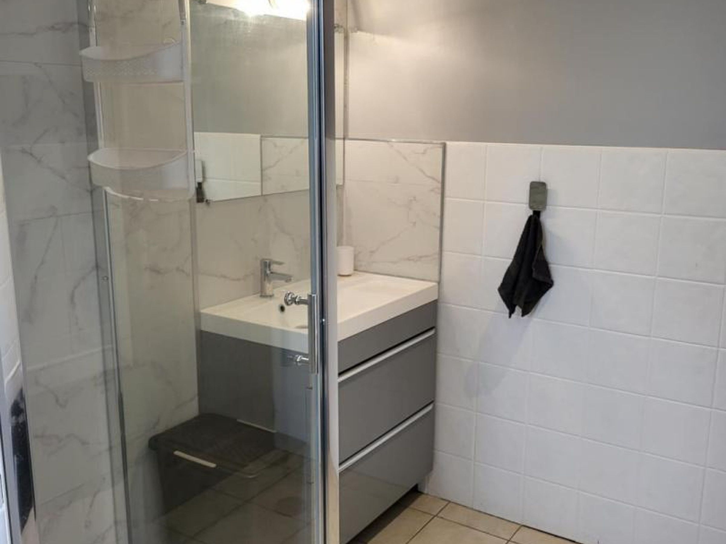 Ein Badezimmer mit Glasdusche, Waschbecken mit Spiegel und Handtuchhalter.