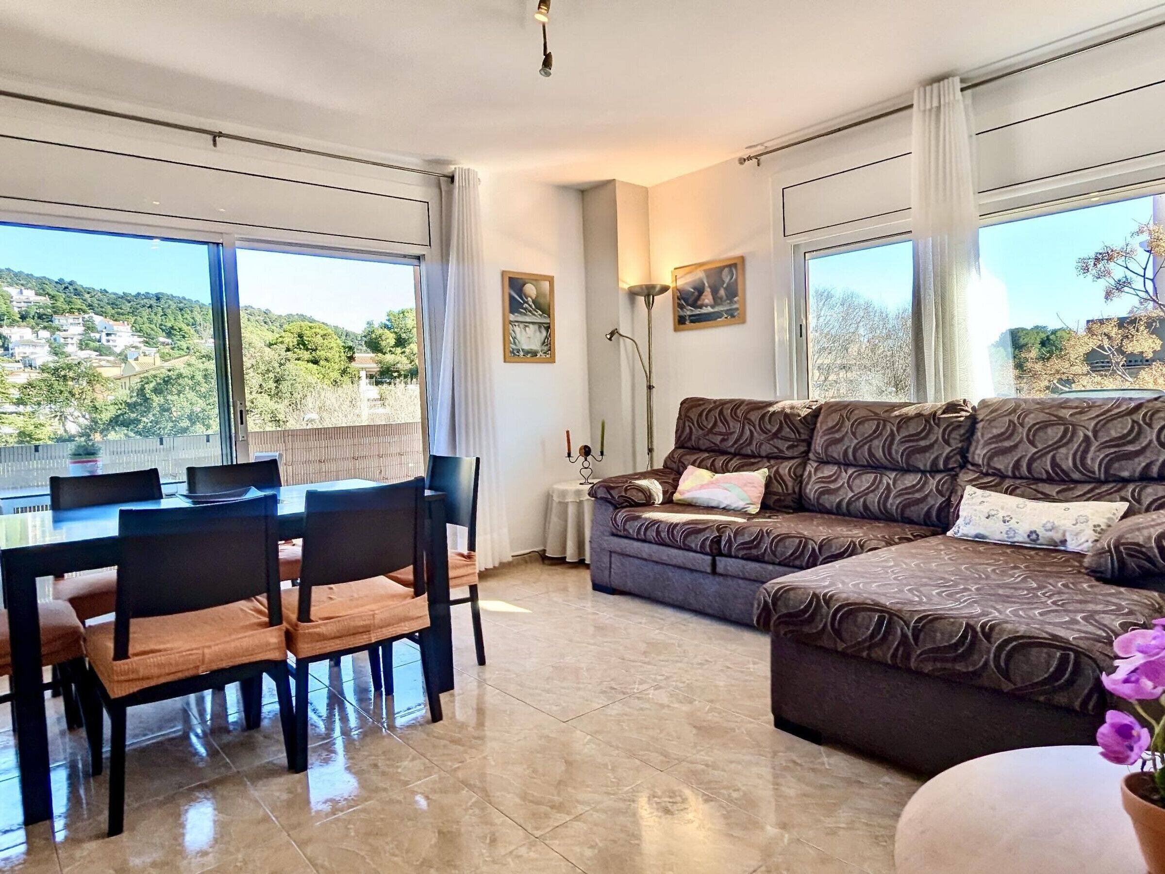 Un salon avec un canapé, une table à manger et des chaises, et une vue sur une colline.