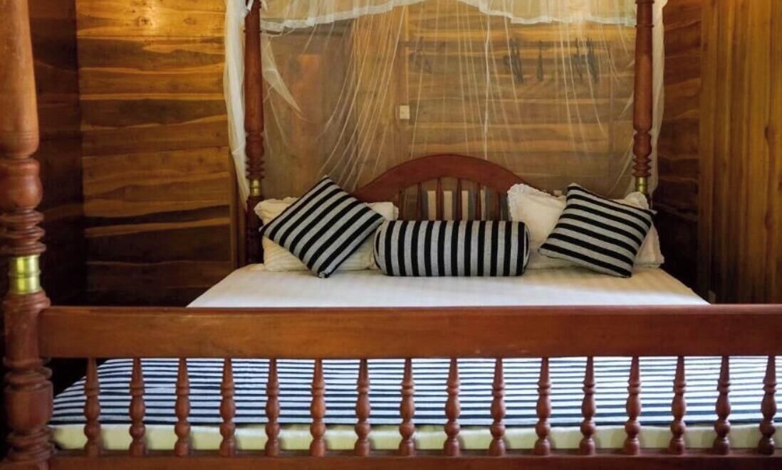 A wooden four-poster bed with a canopy, striped pillows, and a striped mattress.