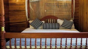 A wooden four-poster bed with a canopy, striped pillows, and a striped mattress.