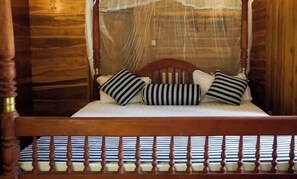 A wooden four-poster bed with a canopy, striped pillows, and a striped mattress.