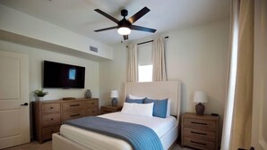 Une chambre à coucher comprenant un lit, des tables de chevet, un téléviseur et un ventilateur de plafond.