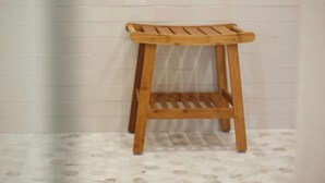Un tabouret en bois, doté d’une assise et d’un dossier à lattes, placé contre un mur recouvert de carreaux.