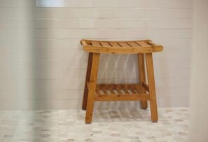A wooden stool with a slatted seat and backrest, positioned against a tiled wall.