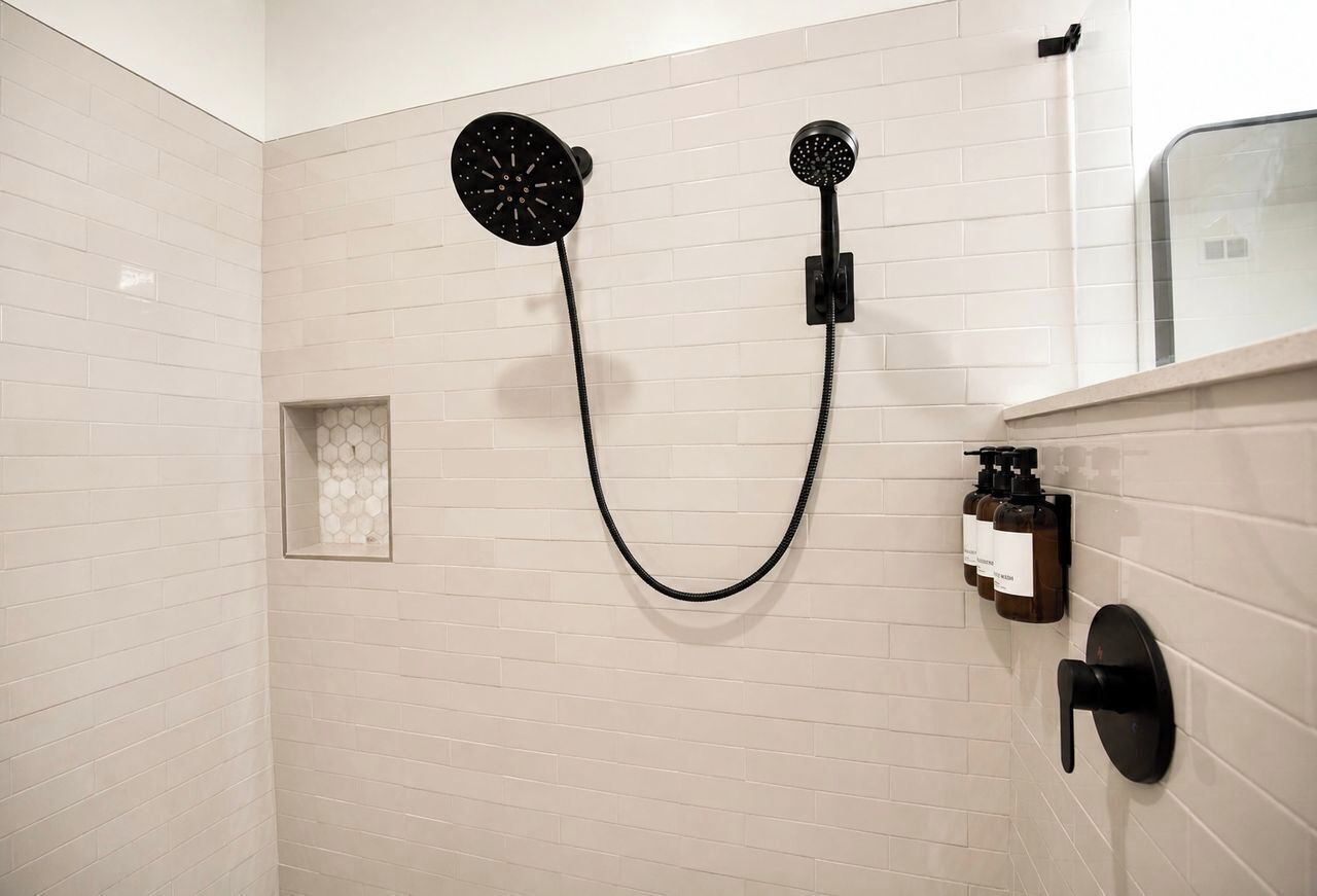 Une douche équipée d’un tuyau noir et de deux pommeaux de douche ronds fixés au mur.