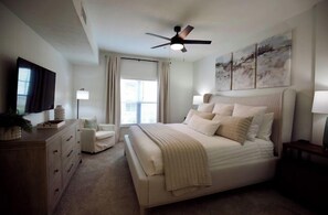 A bedroom with a bed, a ceiling fan, a TV, and artwork on the wall.