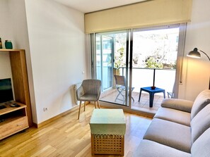 Een moderne woonkamer met een bank, een bijzettafeltje, een stoel en een televisie op een houten dressoir.