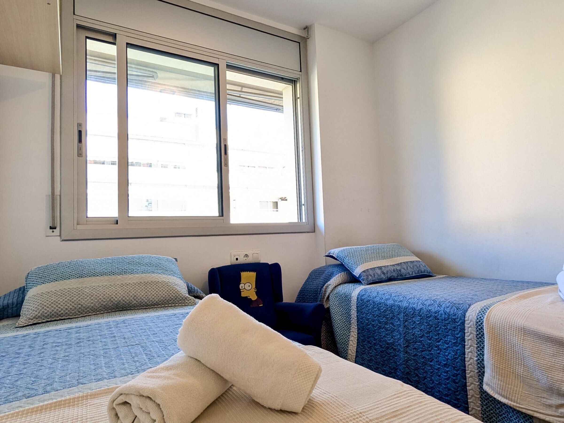 Une chambre avec deux lits, une fenêtre et une prise de courant au mur.
