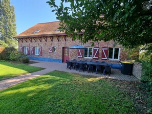 A brick building with a tiled roof, outdoor seating with tables and chairs, and a pathway leading to the entrance.