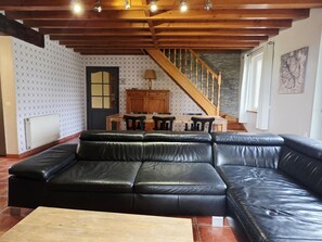 A living room with a black leather sectional sofa, wooden ceiling beams, a dining table with chairs, and a staircase. - Spacious house near Flemish Hills - 14 guests (Méteren)