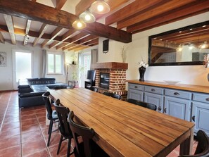 Eine geräumige Küche mit einem langen Holztisch, einem Kamin aus Ziegelsteinen und modernen Leuchten.