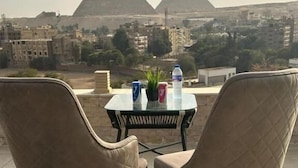 A table with two chairs in front of a view of the pyramids. - city plaza pyramid view (Giza)