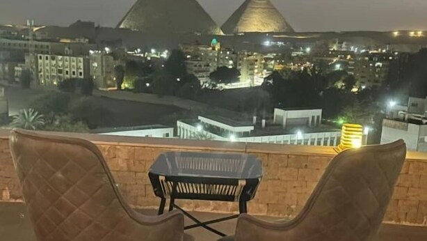 Two cushioned chairs and a small table on an outdoor terrace with a view of pyramids. - city plaza pyramid view (Giza)