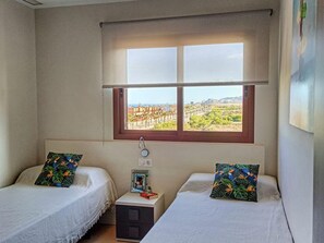 A room with two beds, a window with a view of a landscape, a bedside table with a lamp, and a wall-mounted thermostat. - Charming apartment in San Juan de los Terreros with communal pool and WiFi (San Juan de los Terreros)