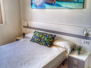 A bed with a white bedspread, a colorful pillow, bedside tables with lamps, and a wall-mounted painting of a boat. - Charming apartment in San Juan de los Terreros with communal pool and WiFi (San Juan de los Terreros)