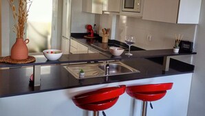 Una cocina moderna con encimera negra, pileta de acero inoxidable y taburetes rojos.