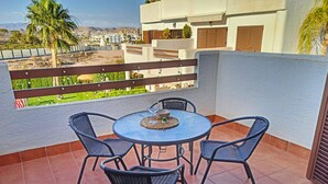 Una terraza con una mesa redonda y cuatro sillas, con vistas a una zona residencial con palmeras y edificios.