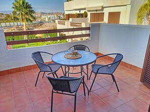 Eine Terrasse mit rundem Tisch und vier Stühlen, mit Blick auf ein Wohngebiet mit Palmen und Gebäuden.